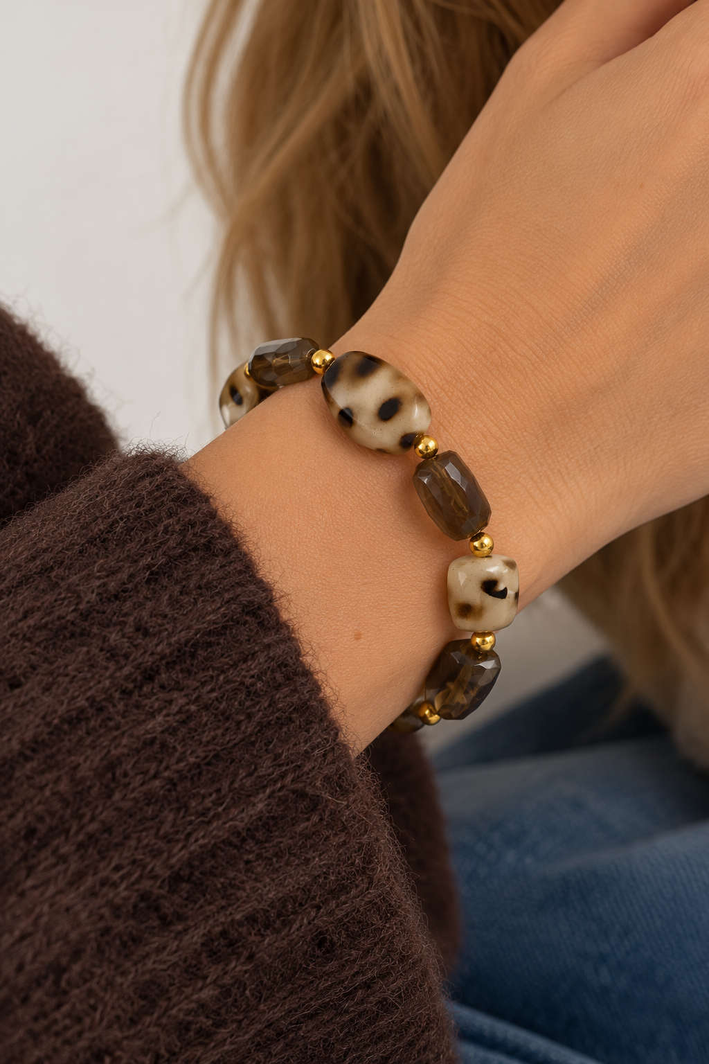 Bruine kralenarmband met gemêleerde beige kralen, transparante bruine kralen en gouden details, gedragen om de pols bij een warme herfstoutfit.